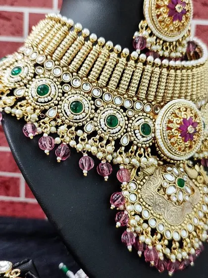 A close-up of a heavy bridal choker for rent. The combination of green stones, magenta beads, and intricate gold-tone work makes this a truly royal piece.