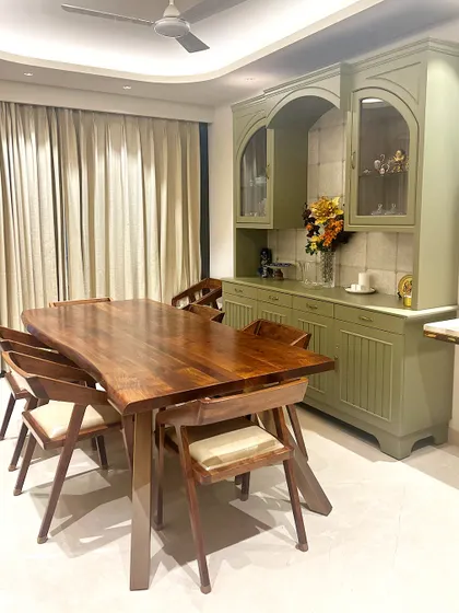 The dining area is anchored by a custom live-edge wooden table, providing an organic contrast to the sophisticated, muted green crockery unit. This space was designed for both family meals and elegant entertaining, balancing functionality with refined aesthetics.