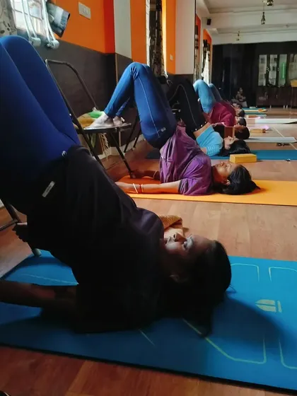 Here we are practicing a supported version of Setu Bandhasana, or Bridge Pose, with our legs resting on chairs. This variation reduces strain on the neck and back while still strengthening the glutes and opening the chest.