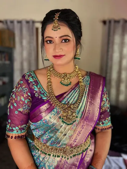 This bride from Mysore looks radiant in a unique peacock-toned silk saree. Her makeup features a soft pink and gold eye look with a matching lip color to complement her intricate floral blouse.
