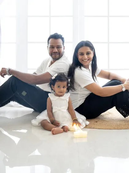 A creative family portrait with the parents sitting back-to-back while their daughter sits in front.