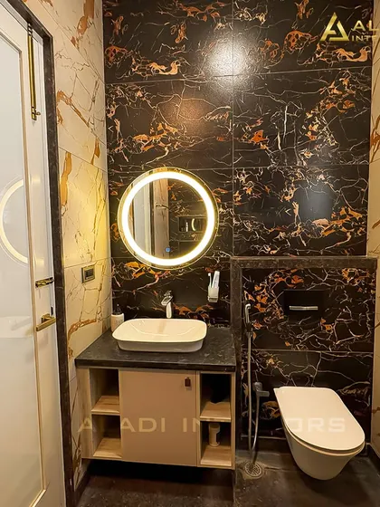 Another view of the black and gold marble bathroom, showing the wall-mounted toilet and the elegant, circular backlit mirror.