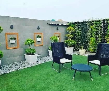 A modern terrace design combining multiple elements for a clean, stylish look. This project features artificial turf, a living wall for privacy, pebble borders, and unique wall art using framed planters to display bonsai trees.