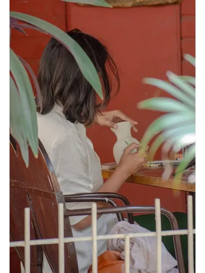 A quiet moment of creativity. A guest is absorbed in painting a vase, finding her flow in our relaxed, leafy outdoor seating area.