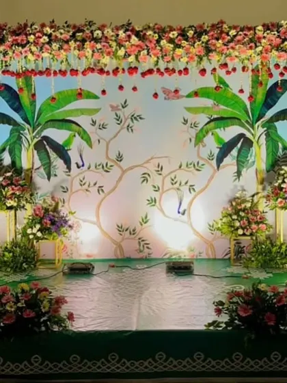 A nature-inspired baby shower backdrop. The hand-painted banana trees and floral vines create a fresh, garden-like feel, complemented by colorful flower arrangements.