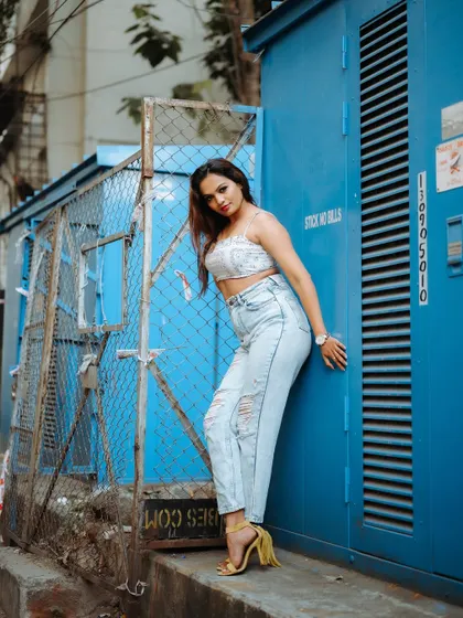 A full-length shot of a model in a casual outfit against a blue industrial background. The composition is clean and highlights her street style.
