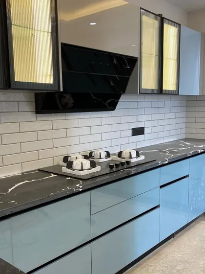 This kitchen features a striking combination of glossy blue cabinets, a black marble-patterned countertop, and a white subway tile backsplash. The fluted glass upper cabinets with internal lighting add a trendy, modern touch.