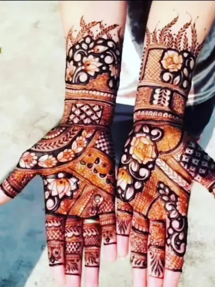 A beautiful henna design with a rich brown stain, perfect for outdoor events. The pattern includes floral motifs and delicate leafy vines at the top of the arms.