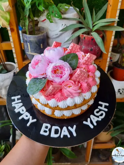 A "naked" Lotus Biscoff mousse cake. The exposed layers are decorated with piped cream, pink chocolates, and faux peonies for a rustic yet chic look.