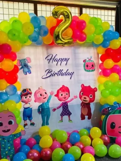 A bright and cheerful Cocomelon theme for a 2nd birthday, featuring a large character backdrop and a rainbow balloon arch.