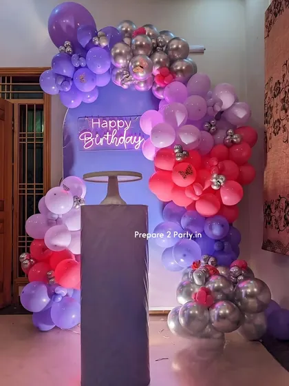 A lovely lavender-themed birthday decoration. This setup features a purple arch backdrop, a neon sign, and a balloon garland in shades of lavender, pink, and silver with butterfly accents.