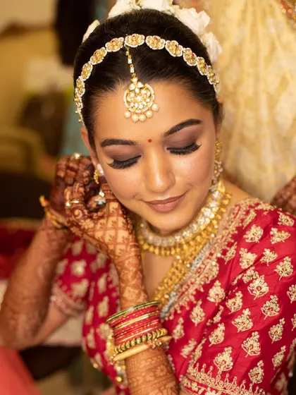 Another glimpse of a bride getting ready. The dark henna stain provides a beautiful contrast against her skin and traditional red attire, completing the classic bridal aesthetic.