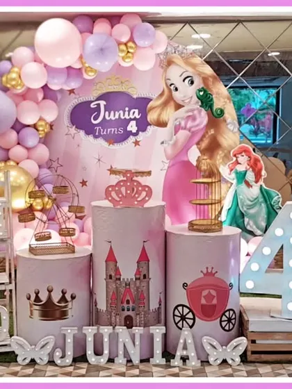 A grand princess-themed fourth birthday party. This setup features cutouts of various Disney princesses like Rapunzel and Ariel, a castle-themed backdrop, and a large light-up number '4'.