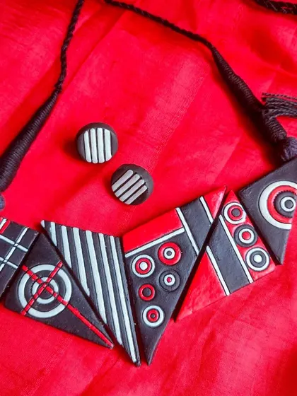 A stunning geometric necklace made of triangular terracotta pieces in red, black, and white. This is a bold, architectural piece for the fashion-forward customer.