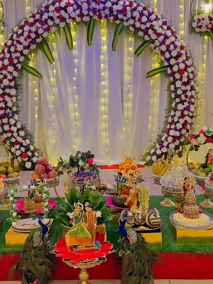A beautiful half-saree function setup with a large floral ring as the backdrop. My gift platters, featuring peacock motifs and personalized cutouts, are perfectly coordinated with the decor.