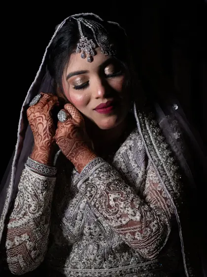 A close-up of a Muslim bride adjusting her earring, highlighting her intricate henna and beautiful makeup.