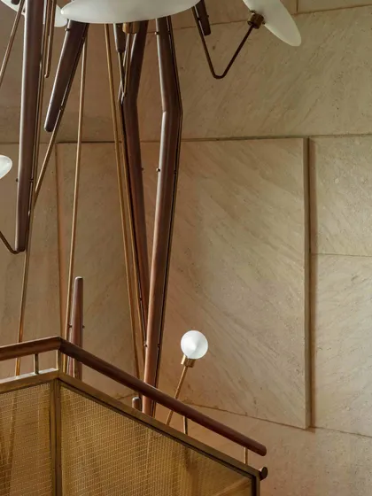 The entrance lobby staircase is a masterpiece of detail, featuring a blend of brass mesh, veneer, and wood. The striking Klove Grasshopper light fixture accentuates the verticality and serves as a dramatic sculptural element.