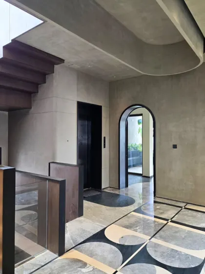 This villa lobby, currently in progress, blends gray microcement walls with a bold geometric marble floor. The arched doorway and sculptural staircase introduce classical and modern forms, creating a space of understated luxury.