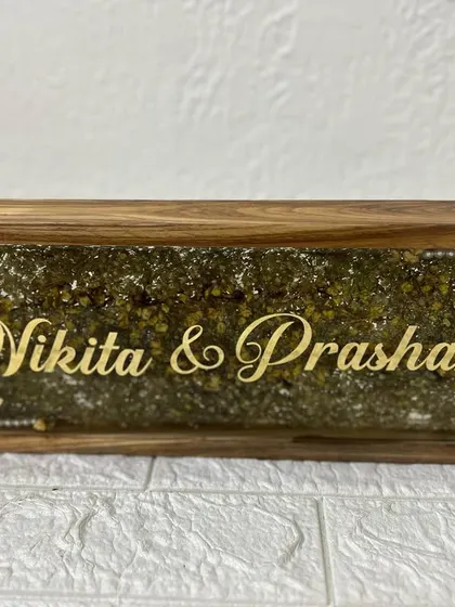 A beautiful wooden frame nameplate, filled with preserved green and yellow flowers. The couple's names in gold script stand out beautifully against the floral background.