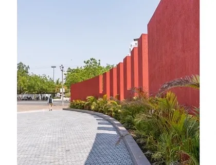 The exterior of the Glass Pavilion, featuring a bold, red, articulated wall that contrasts with the transparency of the main hall. This element serves as both a visual anchor and a guide for circulation.