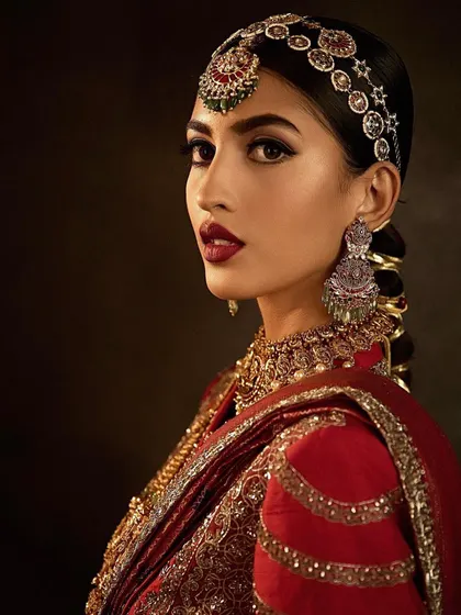 A royal bridal look featuring a deep red lip and antique gold jewelry. This style is about creating a look of pure opulence and timeless elegance, a must-have in any bridal artist's repertoire.