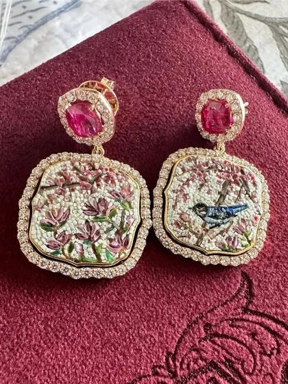 A close up of the cherry blossom earrings, showing a bluebird on a branch. The micromosaic technique allows for such intricate details, creating a wearable piece of art, complemented by natural rubies.