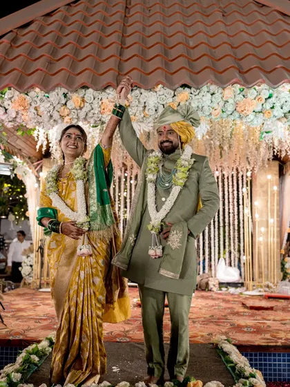 The couple celebrates under the mandap, their hands raised in joy.