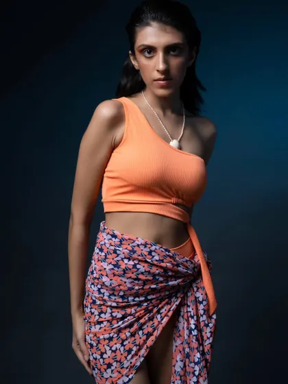 A close-up from the same swimwear campaign. The blue-gelled background light adds a cool tone that complements the orange top, creating a professional, polished look.