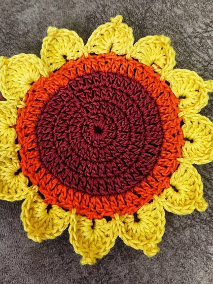 A detailed close-up of a single sunflower coaster. You can see the intricate spiral stitching of the center and the individually crafted petals that make each piece a small work of art.