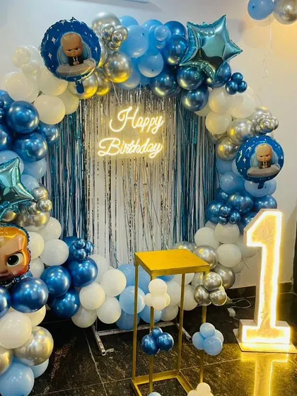 A Boss Baby first birthday party with a blue and silver theme. This circular balloon arch is accented with a shimmer curtain, a neon sign, and a light-up number '1'.
