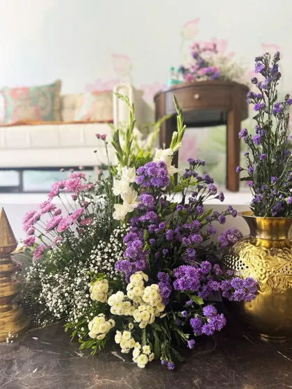 A close-up of a floral arrangement for the spiritual event, with a mix of purple, pink, and white flowers in a golden vase, exuding grace and serenity.