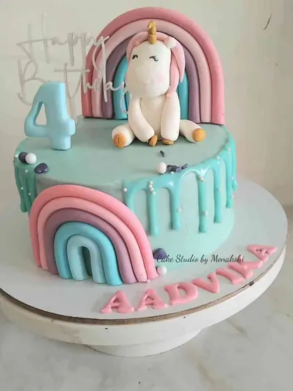 A cute unicorn themed cake with a drip effect. This design features a unicorn sitting beside a pastel rainbow, perfect for a 4th birthday.