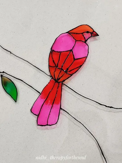A close-up of a pink and red bird being painted on the glass. The colors are applied to create a faceted, geometric look.