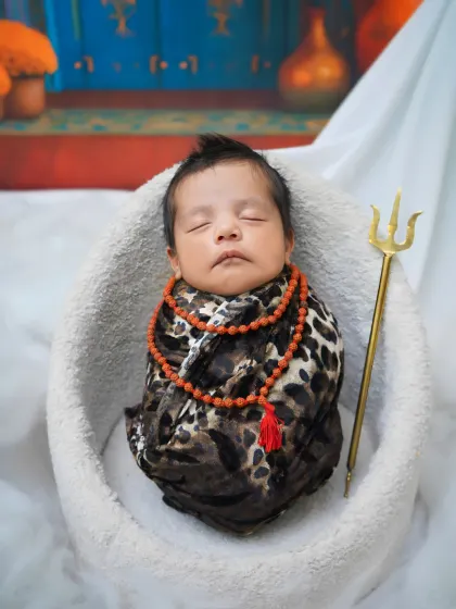 A close-up of the 'Little Shiva' newborn theme. This shot details the rudraksha beads, leopard-print swaddle, and mini trishul, capturing a divine and peaceful portrait.