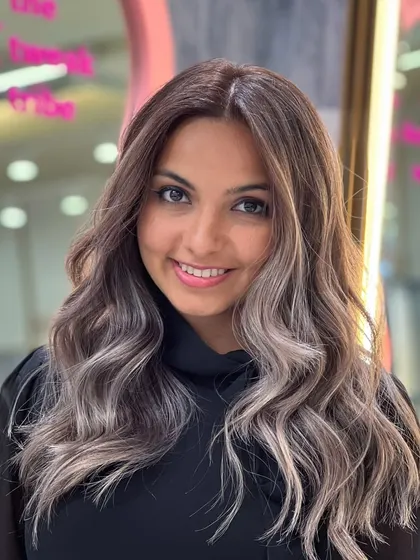 A smiling client showing off her new signature balayage. The cool, ashy tones and face-framing highlights create a stunning and modern look.