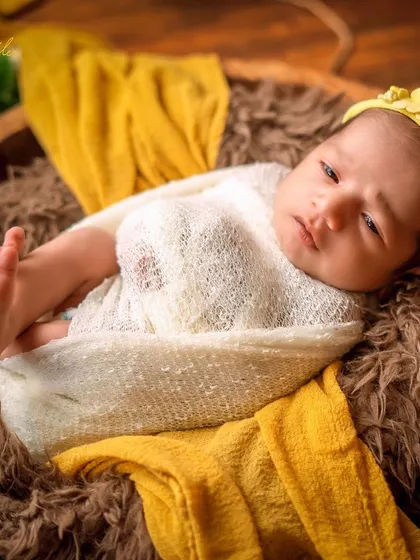 An alert and curious expression from a baby nestled in a wooden bowl. The contrast of the bright yellow headband and the rustic props makes this shot pop.