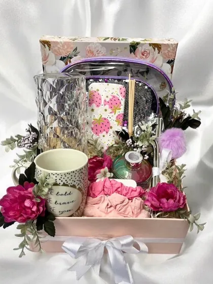 One of our Rakhi hamper designs. This one is packed in a floral box and filled with a variety of goodies for her, including a mug, a vase, and beauty items, all arranged with artificial flowers.