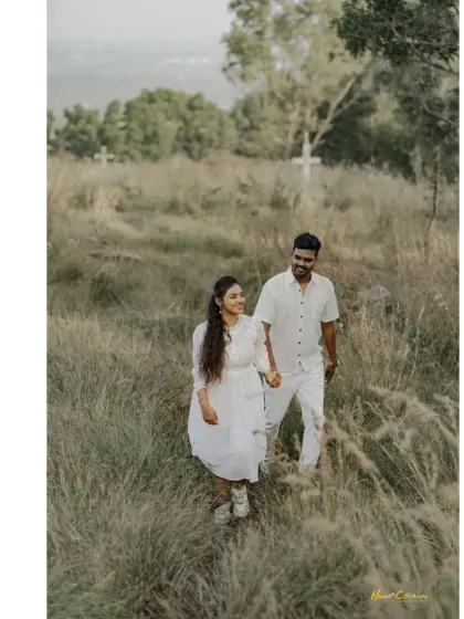 A couple walks hand-in-hand through a field of tall grass, sharing a smile. A perfect candid moment from a nature-filled pre-wedding shoot.
