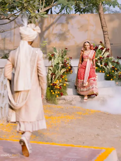 The groom walks towards his bride, who waits for him at the top of the steps, a moment of anticipation before they unite.