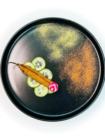 A single bharwan mirch, or stuffed chili, is presented with artistic flair. It is filled with a goat cheese mousse and served with a chilli aam papad chutney, balancing spice with creamy and tangy notes.