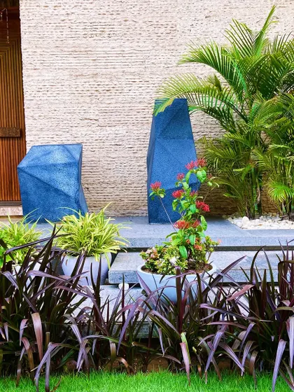 An elegant villa entrance in Faridabad, featuring geometric blue planters, lush palms, and a border of deep purple foliage.