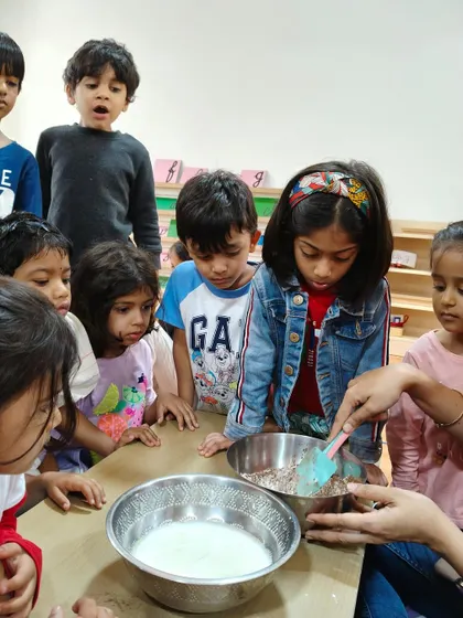 A group of children watch with fascination as the wet and dry ingredients are combined. They are learning about chemistry and transformation in a delicious way.