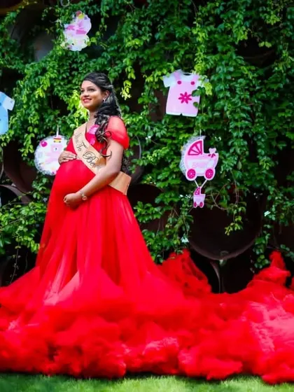A cute and fun outdoor baby shower theme for a maternity shoot. The bright red gown stands out beautifully against the lush greenery and festive decorations.