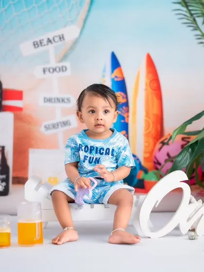 A classic portrait from a beach-themed milestone session. The setup includes "One" lettering to mark the special occasion alongside fun, tropical props.