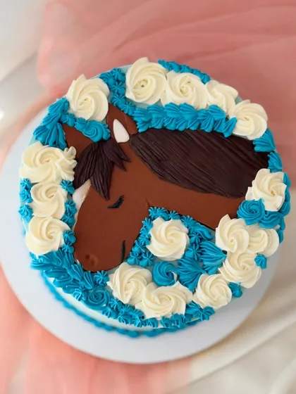 For the horse lover, this cake features a horse portrait created with buttercream piping. The surrounding blue and white rosettes frame the design beautifully.