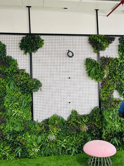 The installation process of a vertical garden. The artificial plant panels are attached to a wire mesh frame on the wall.