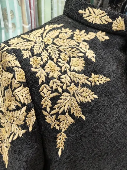 A detailed close-up of the gold leaf hand embroidery on the black Jodhpuri suit, showcasing the texture and precision of the zardozi work.