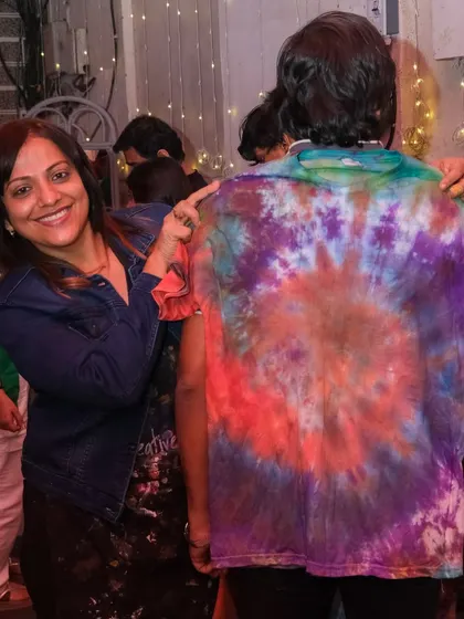 A smiling participant points to the back of a brightly colored tie-dye shirt, a fantastic result from one of our group craft events.