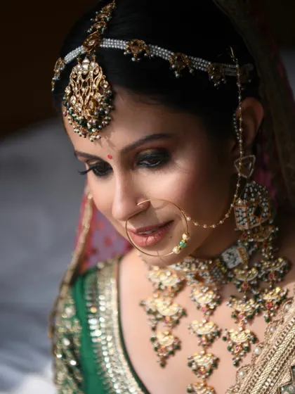 An intricate bridal look featuring heavy Polki jewellery with green accents. The eye makeup is a dramatic smokey look, balanced with a neutral lip color to let the jewellery stand out.