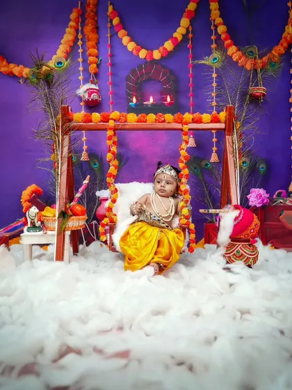 A full view of the Radha theme setup, with a beautiful swing decorated with marigold garlands and peacock feathers against a rich, festive background.